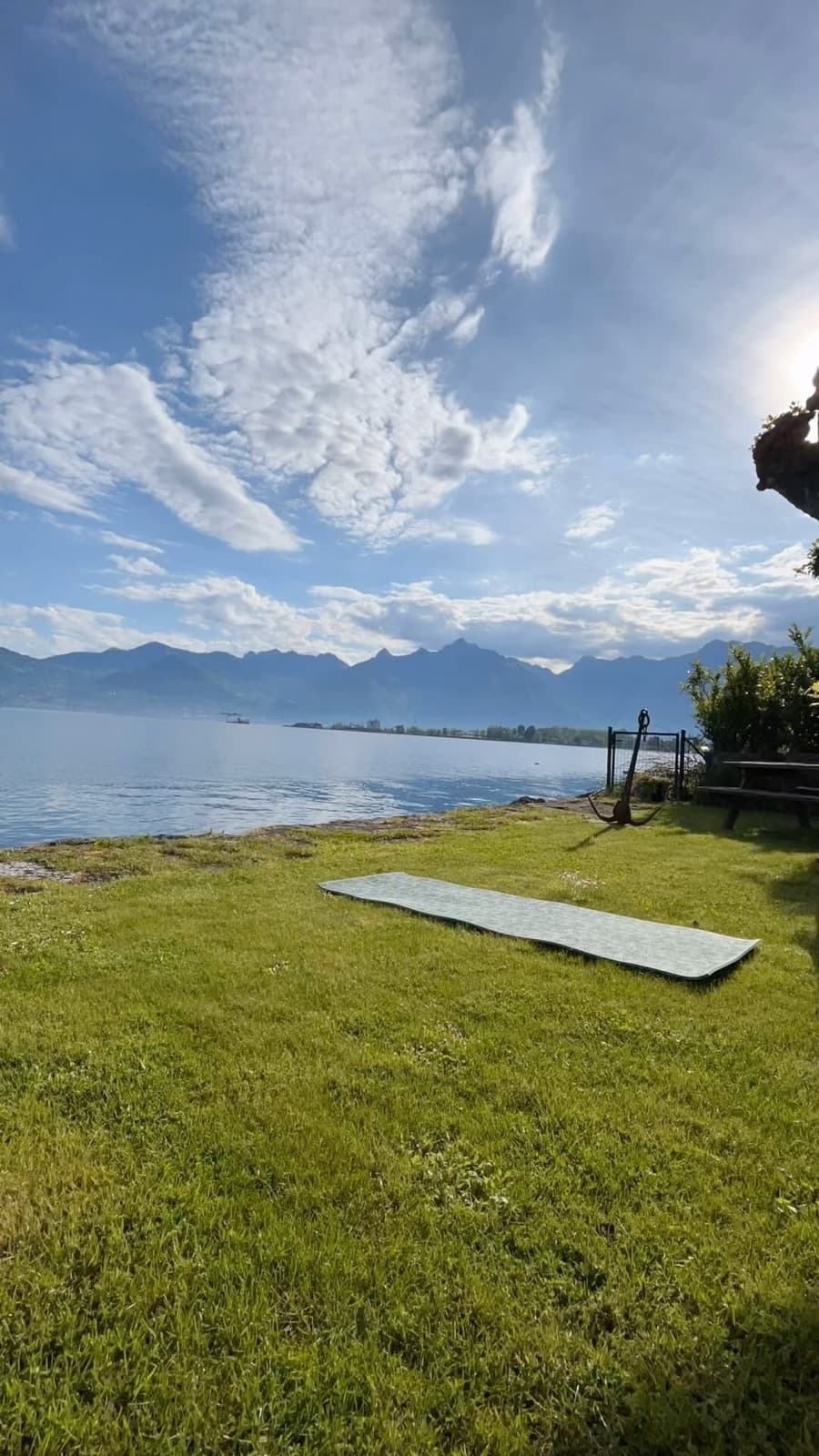 Un tapis de yoga déroulé sur la pelouse au bord du Léman, face aux montagnes, sous un grand ciel bleu