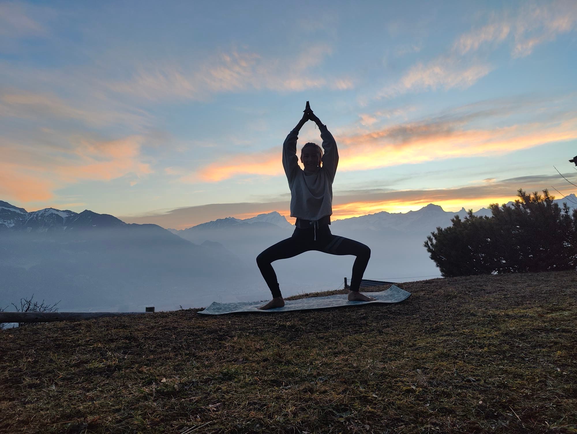 Léa en posture de la déesse sur un tapis de yoga, au lever du soleil, au-dessus d'une mer de brouillard et des montagnes