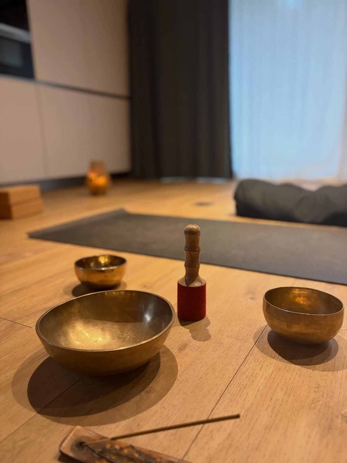 Des bols chantants et leur mailloche posés sur un parquet, devant un tapis et un coussin