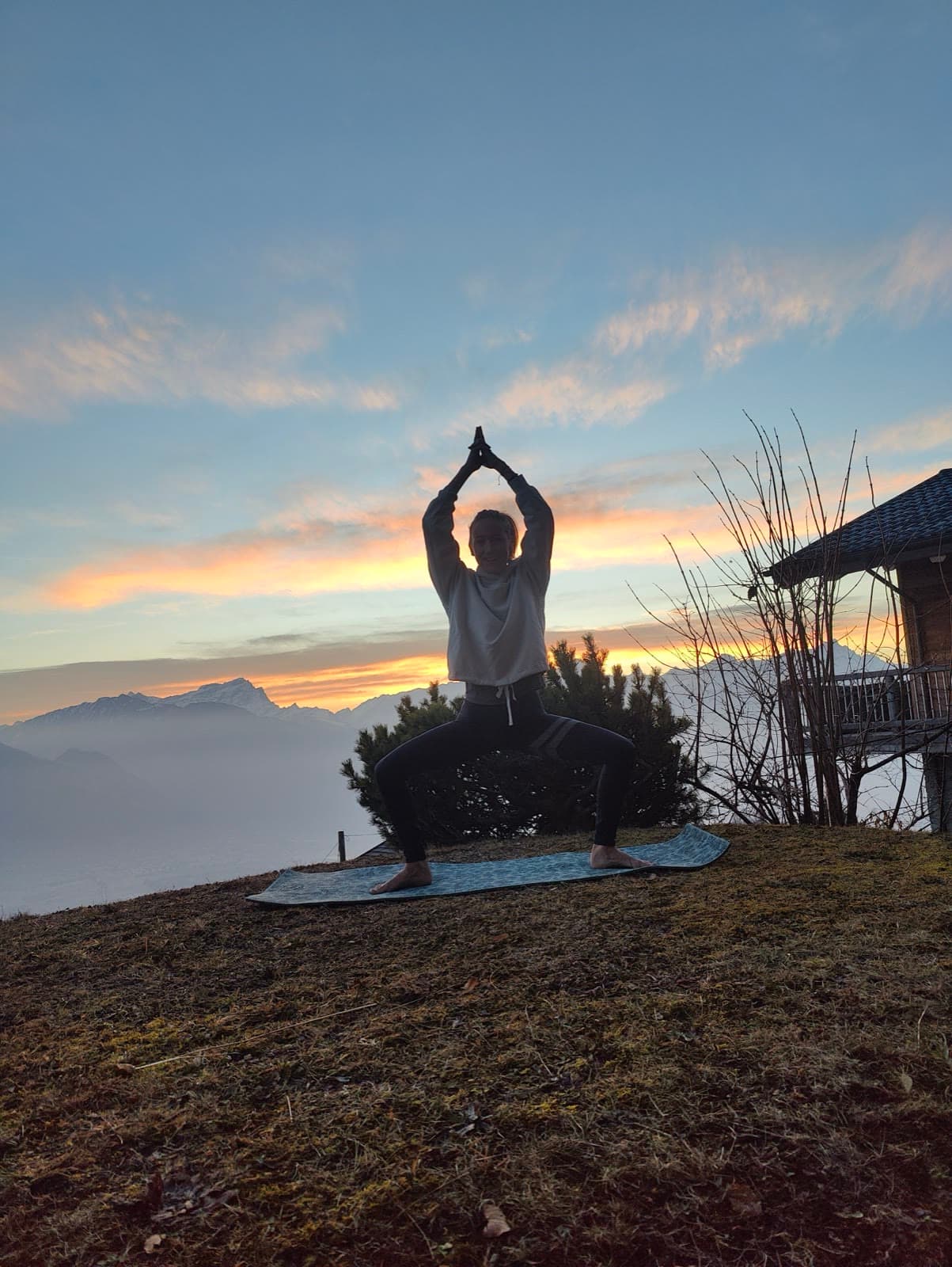 Léa en posture de la déesse dans un pré de montagne, au lever du soleil
